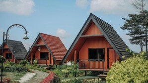 A row of red-roofed cottages with balconies, surrounded by greenery and a stone pathway. - The Kotenang (Wonosobo)