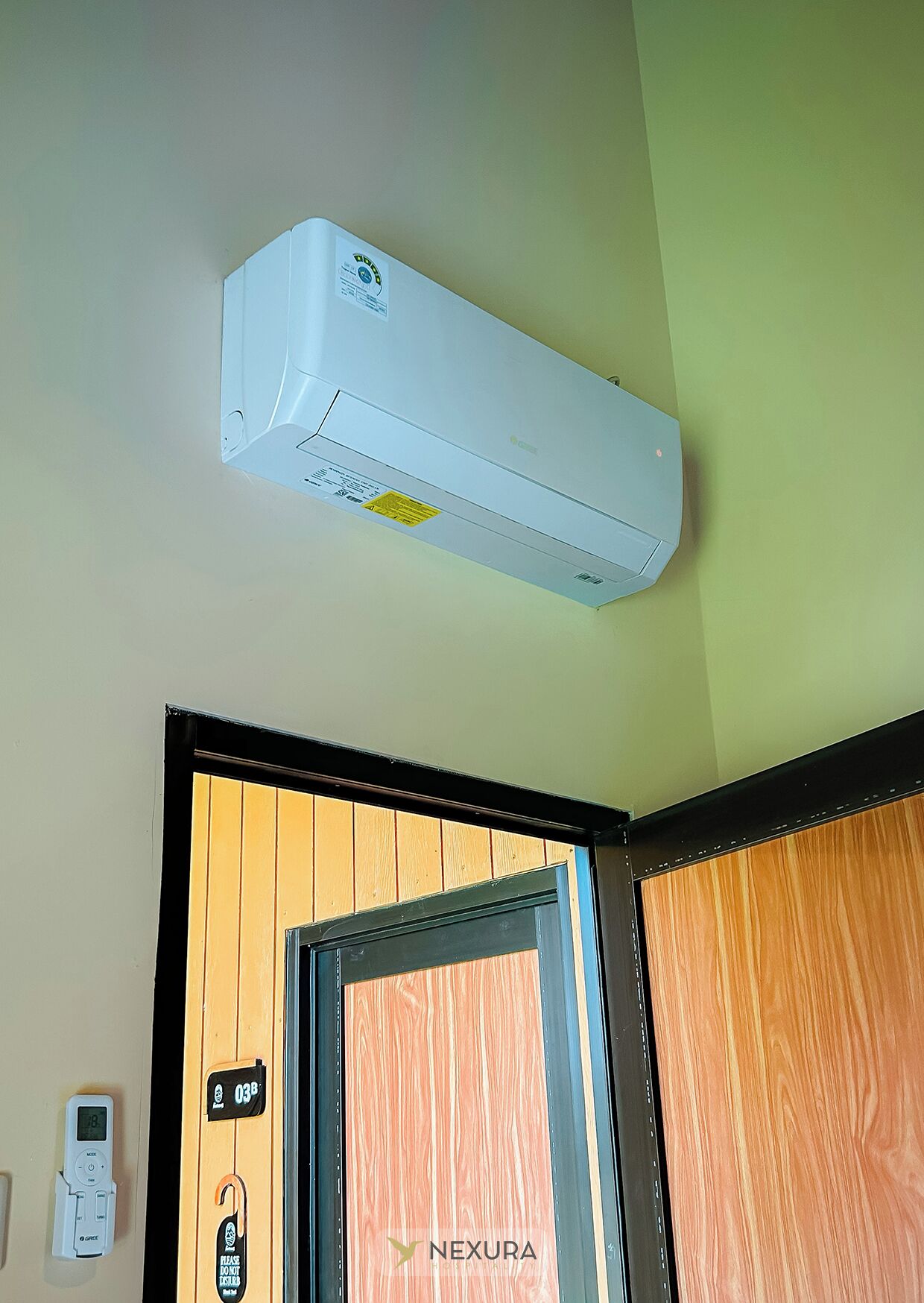 Una unidad de aire acondicionado blanca montada en una pared, una puerta con detalles de madera y un termostato digital en la pared.