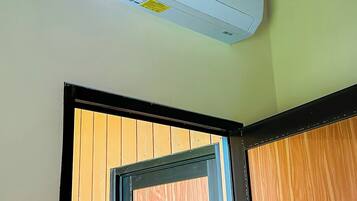 Una unidad de aire acondicionado blanca montada en una pared, una puerta con detalles de madera y un termostato digital en la pared.