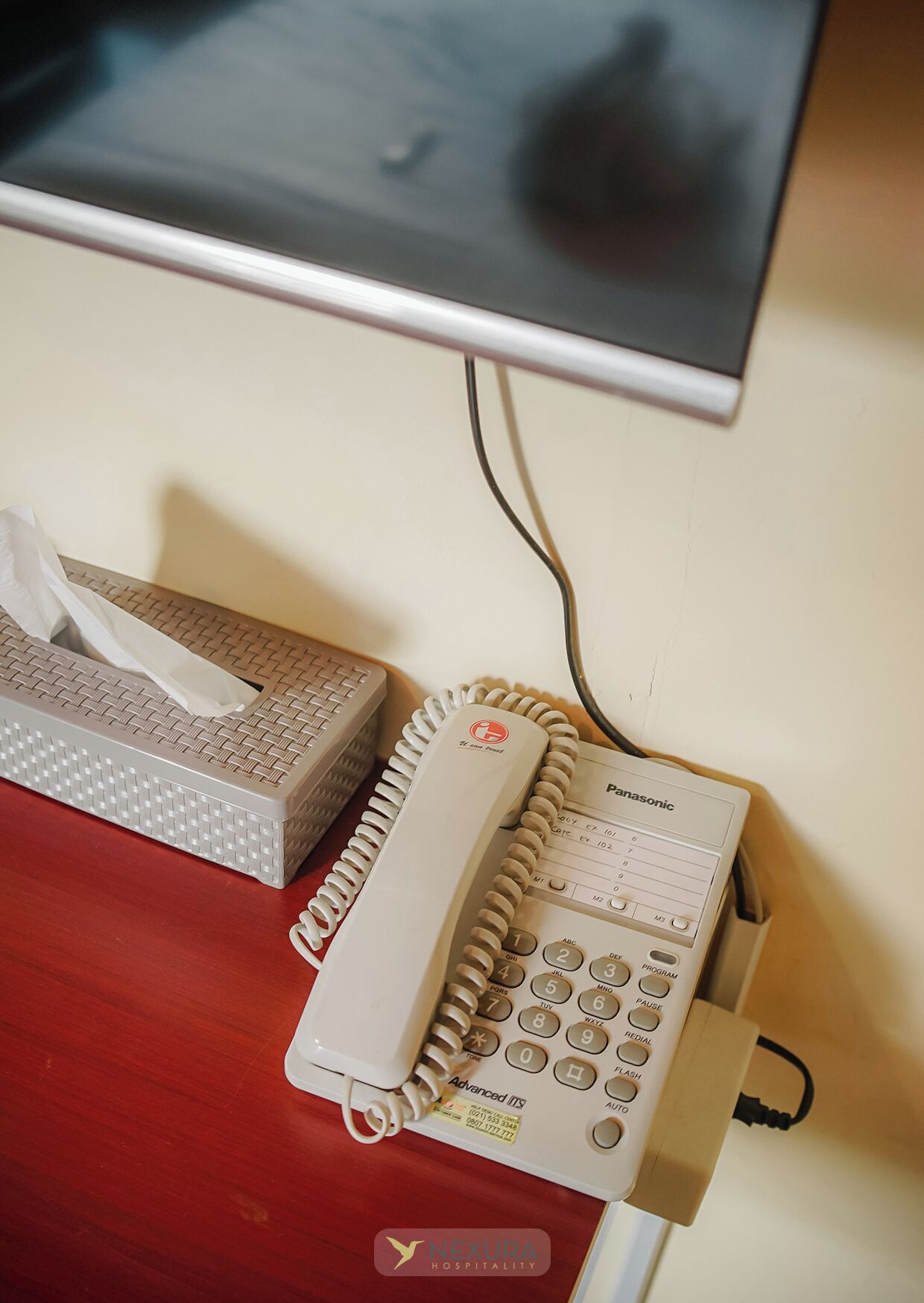 Un bureau avec un téléphone, une boîte de mouchoirs et un écran d’ordinateur.