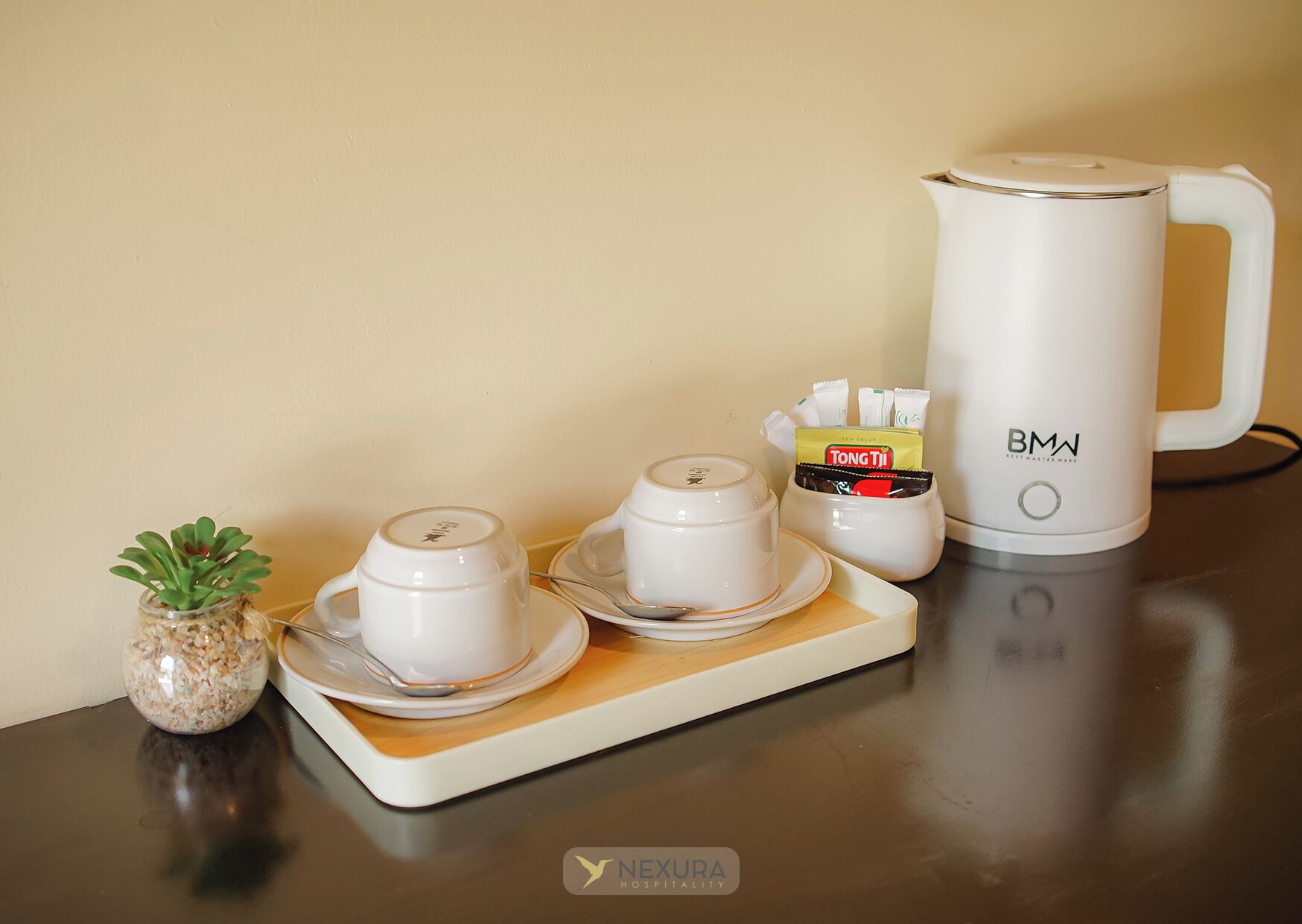 A tea set with a kettle, cups, and a small plant on a table.