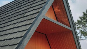 A modern house with a sloped roof, a wooden balcony, and a small outdoor seating area. - The Kotenang (Wonosobo)