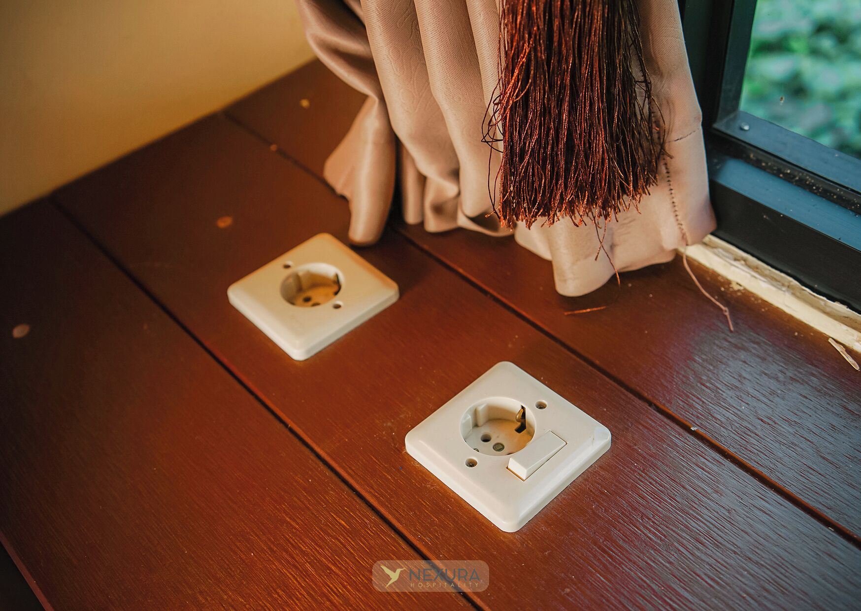 Una mesa de madera con dos tomas de corriente y una ventana con cortina.