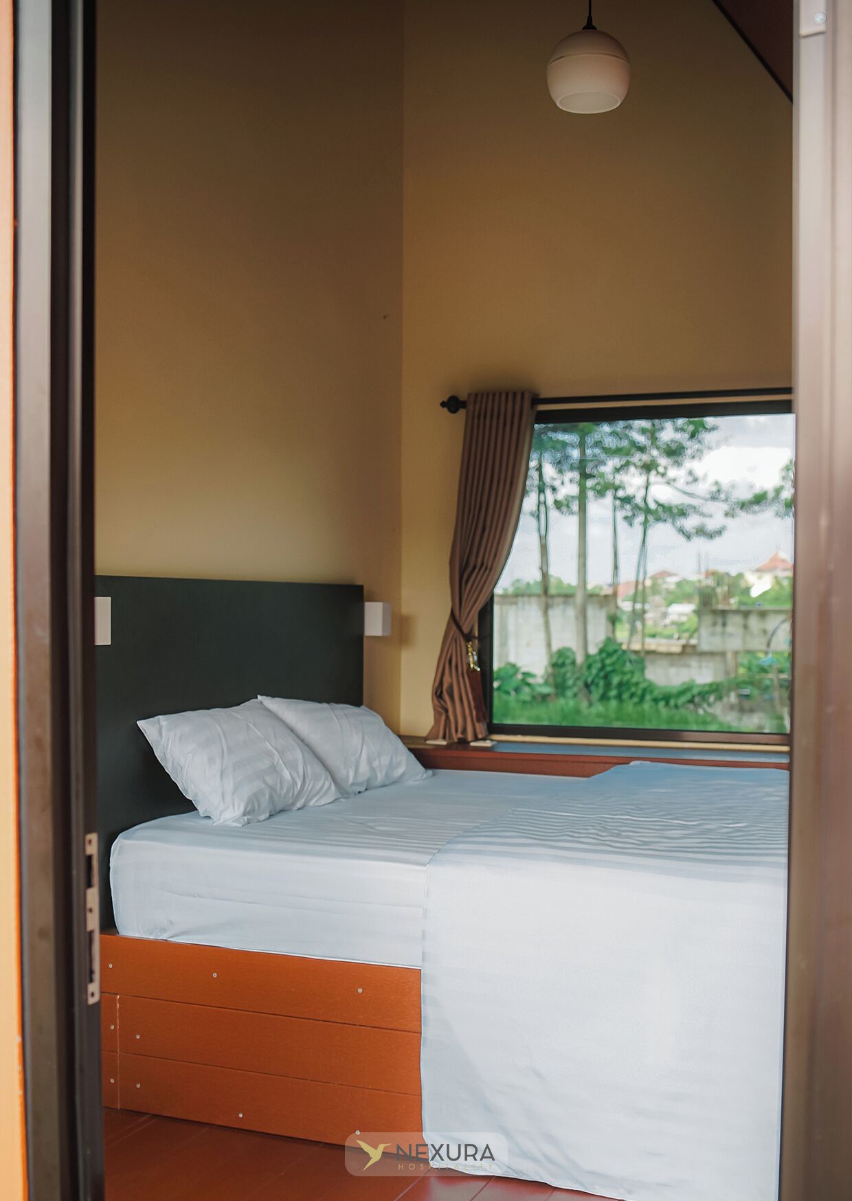 Ein Schlafzimmer mit Bett, einem Fenster mit Vorhängen und einer Pendelleuchte.