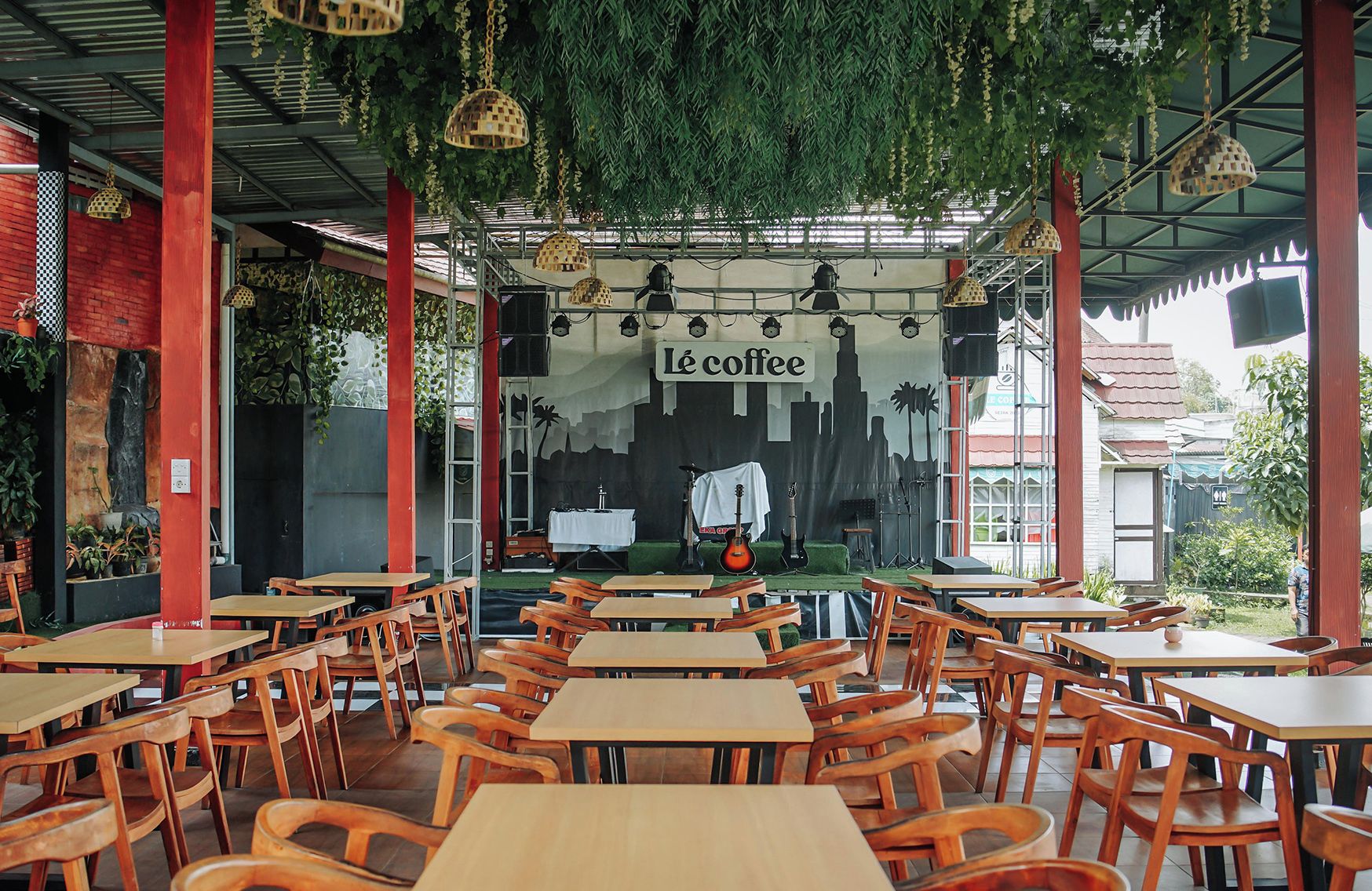 An outdoor café with wooden tables and chairs, a stage with musical instruments, and a mural with 'Le coffee' text.