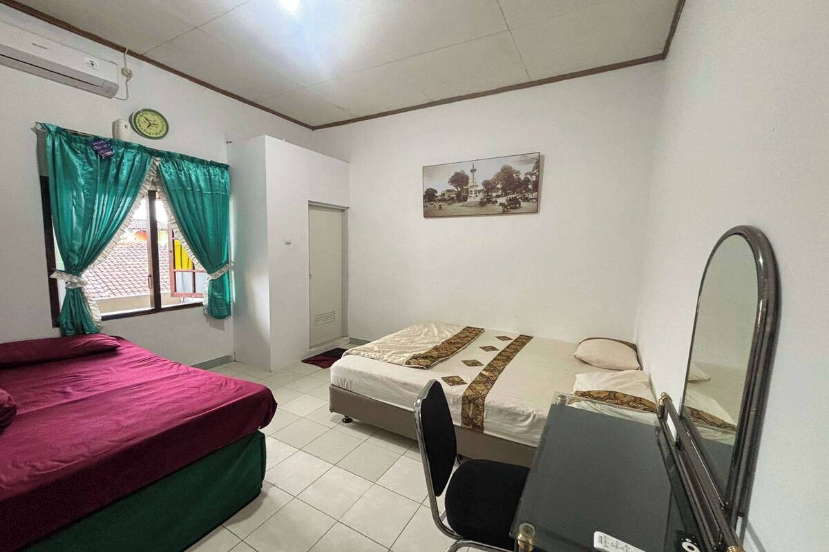 A bedroom with two beds, a desk, a chair, a mirror, and a clock on the wall.