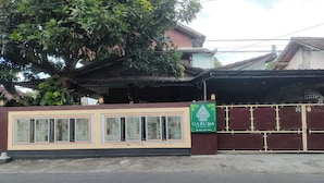 Un bâtiment avec un grand arbre devant, une entrée fermée par un portail et une enseigne indiquant « GARUDA HOMESTAY ».
