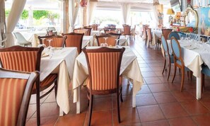 En restaurant med borde dækket til spisning, stole og et flisegulv.