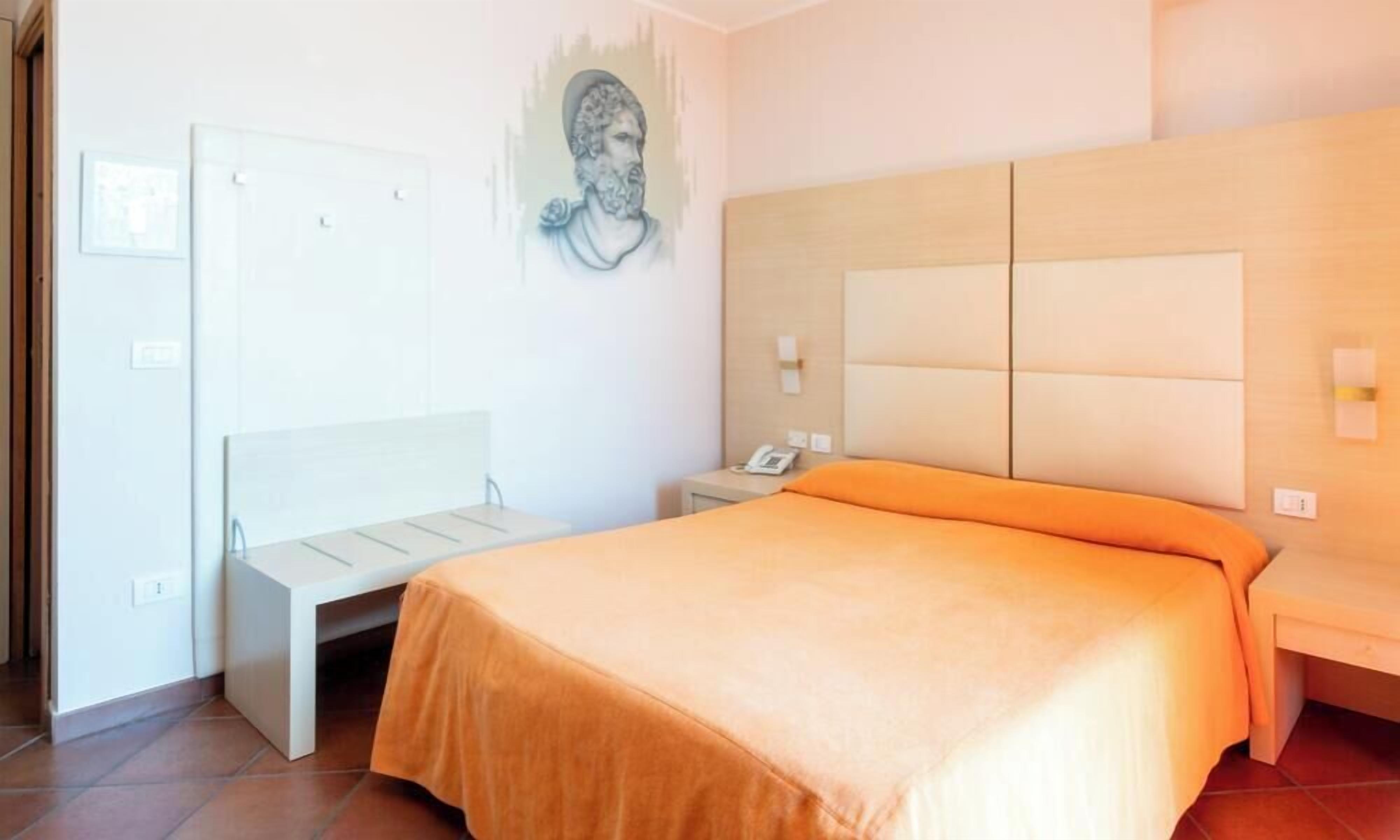 Una habitación de hotel con una cama, una mesita de noche, una silla, una obra de arte en la pared y una puerta.
