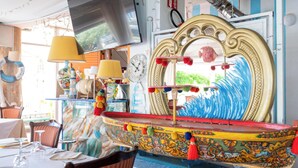 Un comedor con mesas, sillas, televisor, objetos decorativos y un espejo grande.