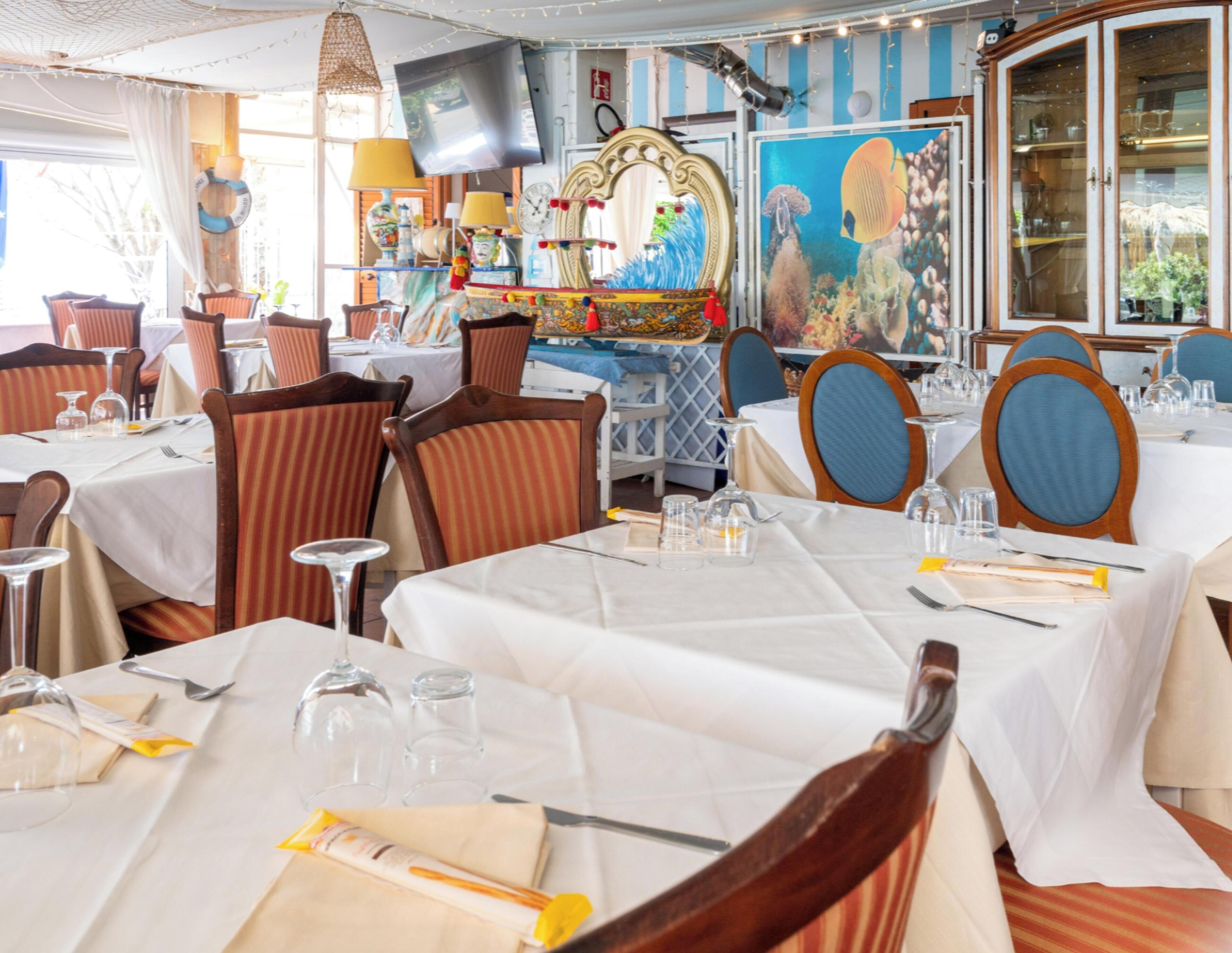 Un interno ristorante con tavoli apparecchiati per consumare i pasti, sedie con rivestimento a righe e un televisore montato a parete.