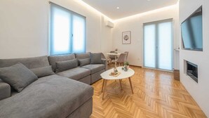 Ein modernes Wohnzimmer mit einem grauen Sofa, einem kleinen weißen Couchtisch und einem an der Wand montierten Fernseher.