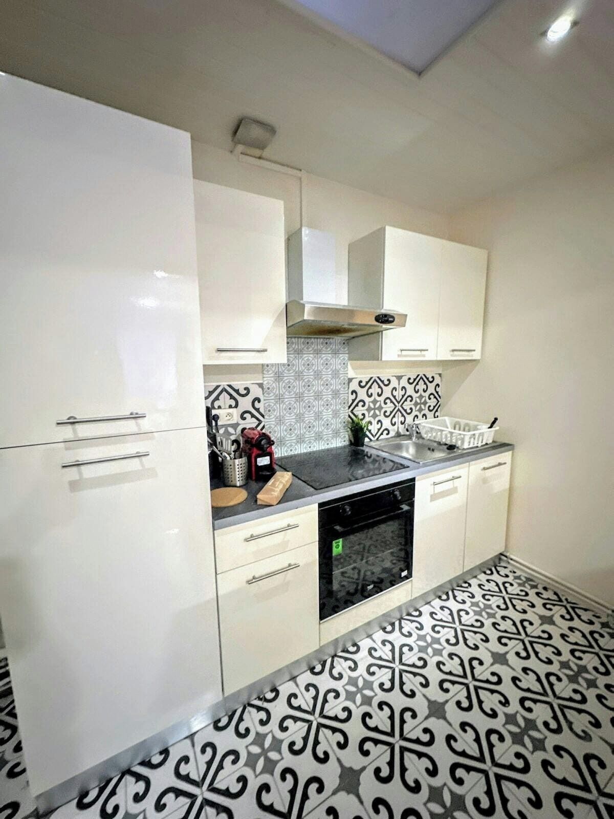 Une cuisine avec des meubles blancs, un four noir et des carreaux de sol à motifs.