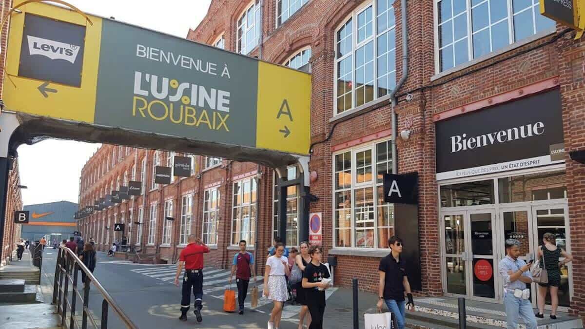 A street sign indicating 'Bienvenue à L'Usine Roubaix' with directional arrows.