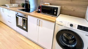 Eine kompakte Küche mit weißen Schränken, einem eingebauten Backofen, einer Mikrowelle und einer Frontlader-Waschmaschine.