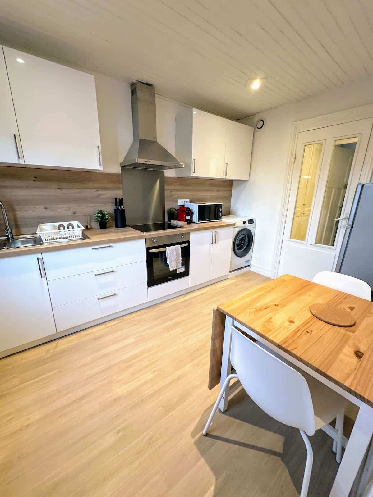 A modern kitchen with white cabinets, a stainless steel range hood, a microwave, and a washing machine.