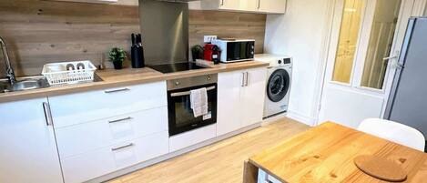 A modern kitchen with white cabinets, a stainless steel range hood, a microwave, and a washing machine.