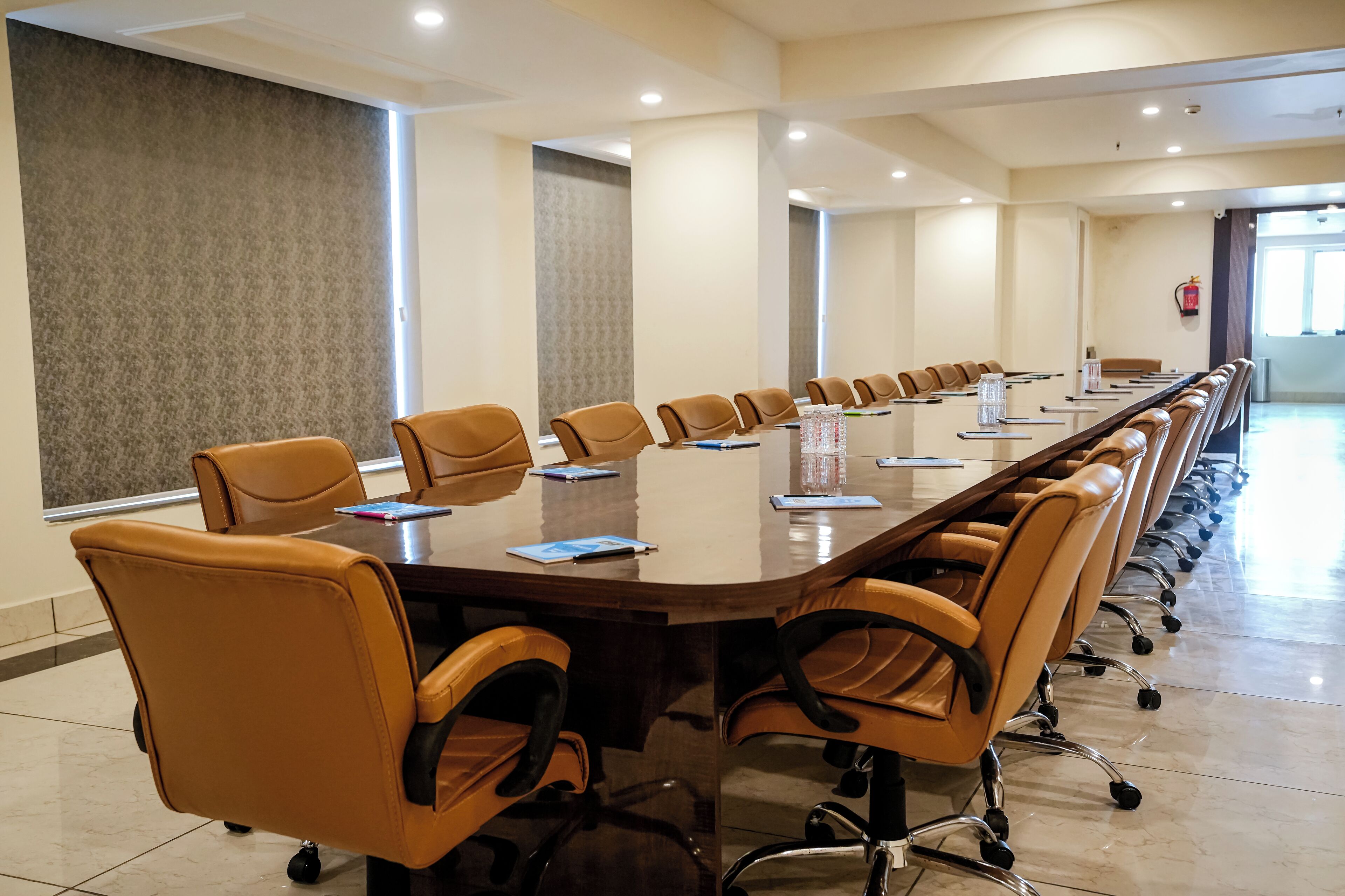 A conference room with a long table, multiple chairs, and a fire extinguisher on the wall.