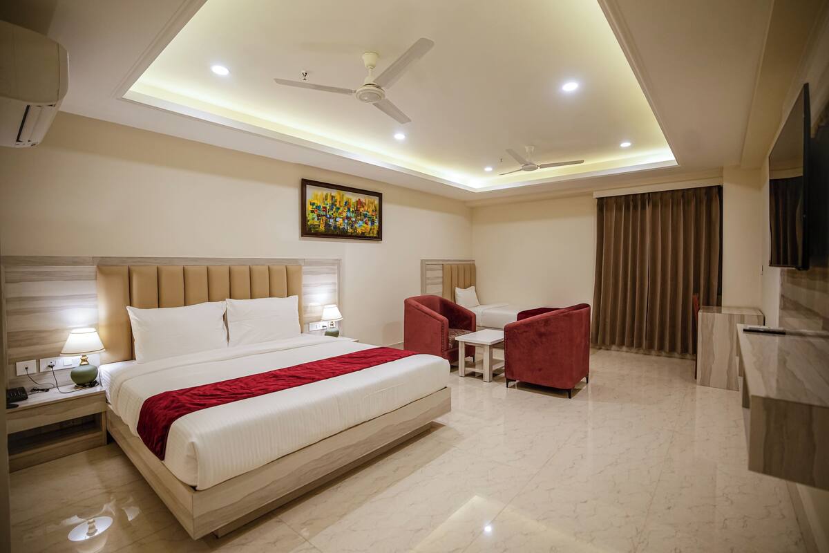 A hotel room with a large bed, two armchairs, a small table, a TV, and a ceiling fan.
