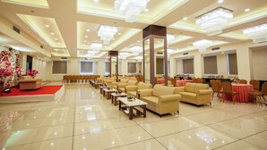 Eine großzügige Hotelhalle mit mehreren Sitzbereichen, darunter Sofas und Tische, und einem roten Teppich, der zu einer Bühne führt.