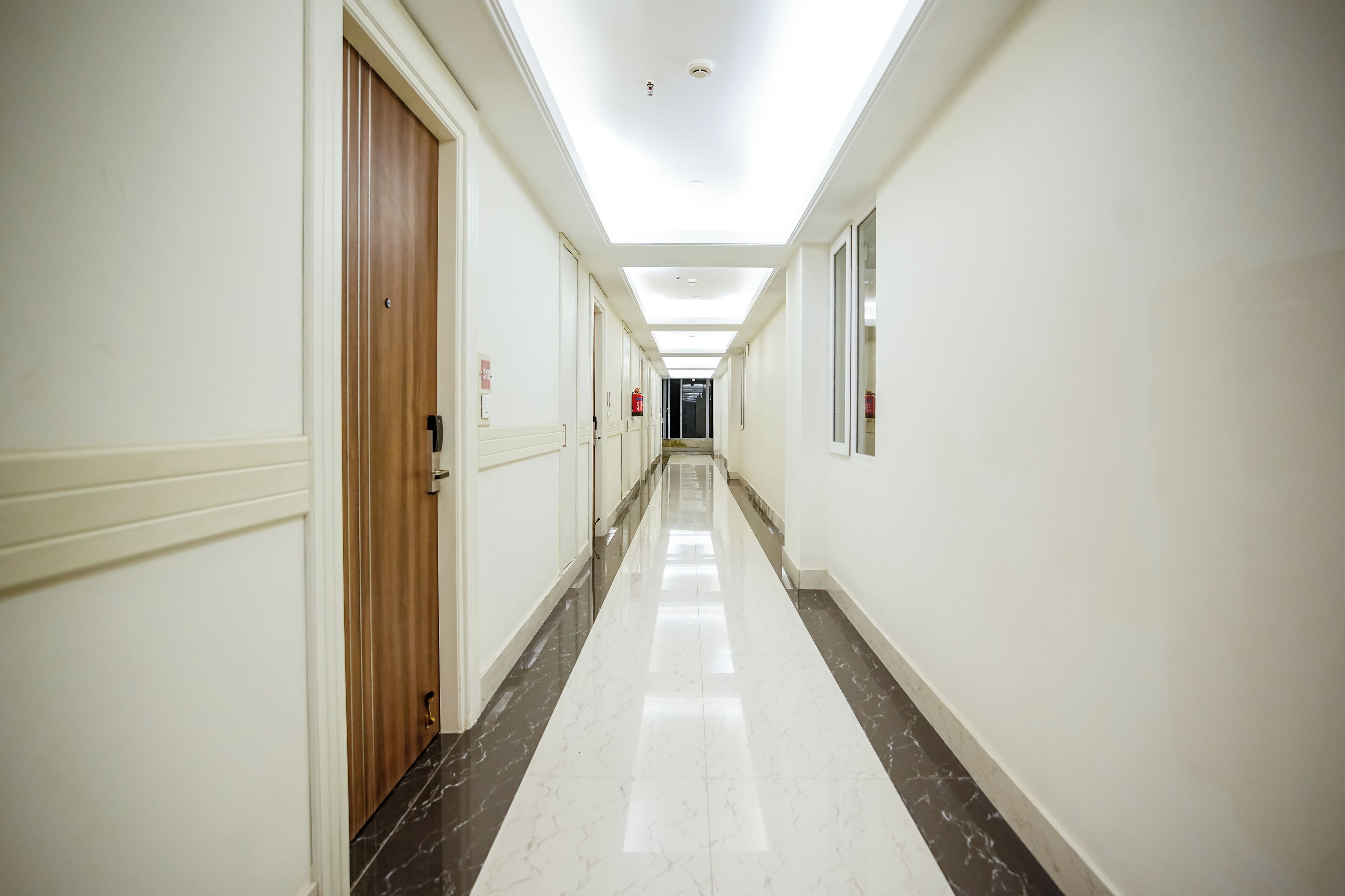 A long, narrow hallway with white walls and a marble floor.