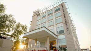 Ein mehrstöckiges Hotel mit einer markanten Eingangspartie, großen Fenstern und einem überdachten Bereich mit Topfpflanzen.