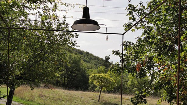 An outdoor dining area with a table set for two, surrounded by white chairs, under hanging lamps. - Domaine la Pause in Aveyron, country house - ideal for families or friends (Vabres-l'Abbaye)