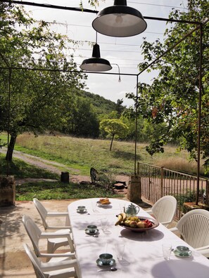 An outdoor dining area with a table set for two, surrounded by white chairs, under hanging lamps. - Domaine la Pause in Aveyron, country house - ideal for families or friends (Vabres-l'Abbaye)