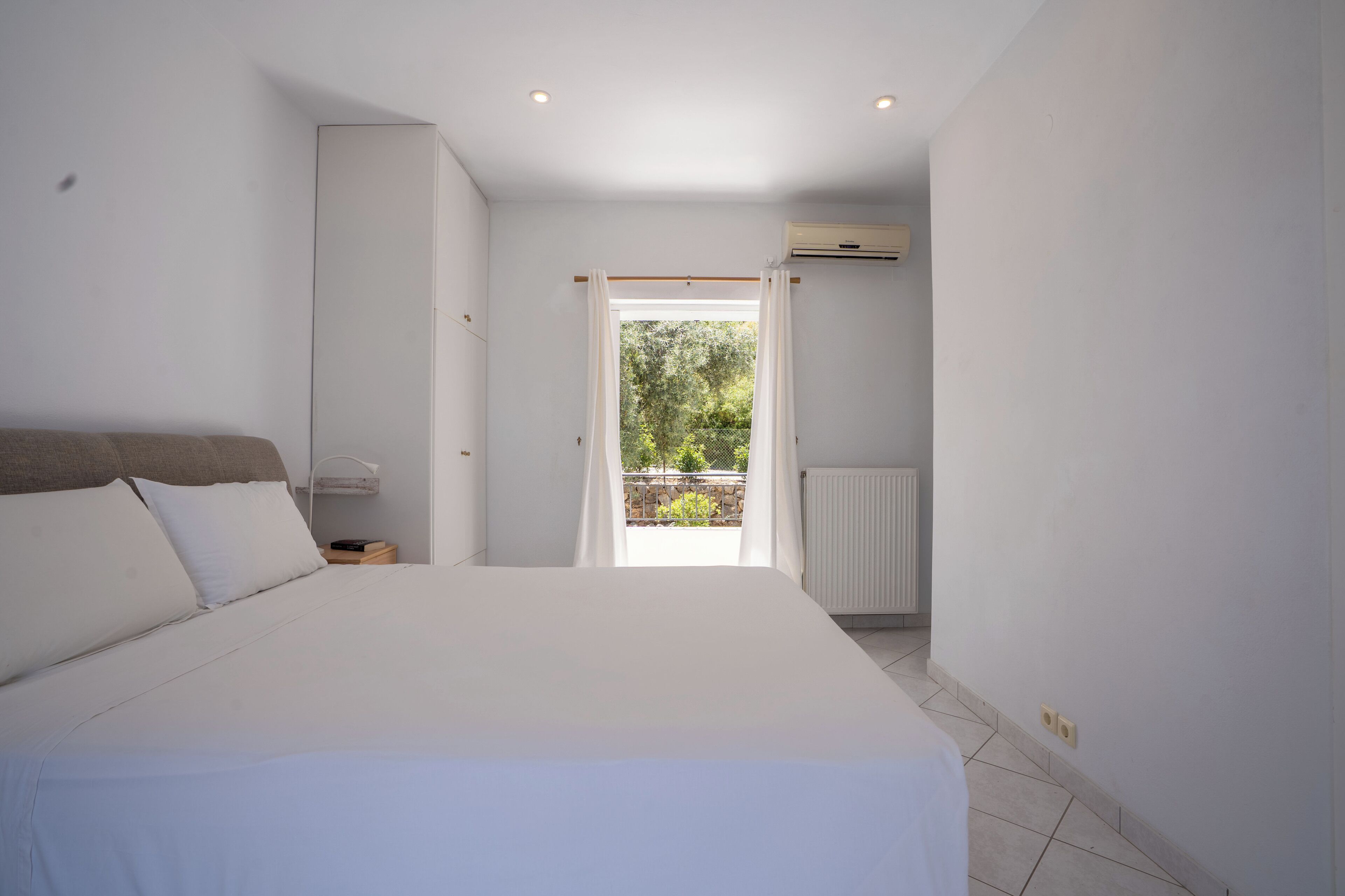 A bedroom with a large bed, a radiator, and a view of the outdoors.