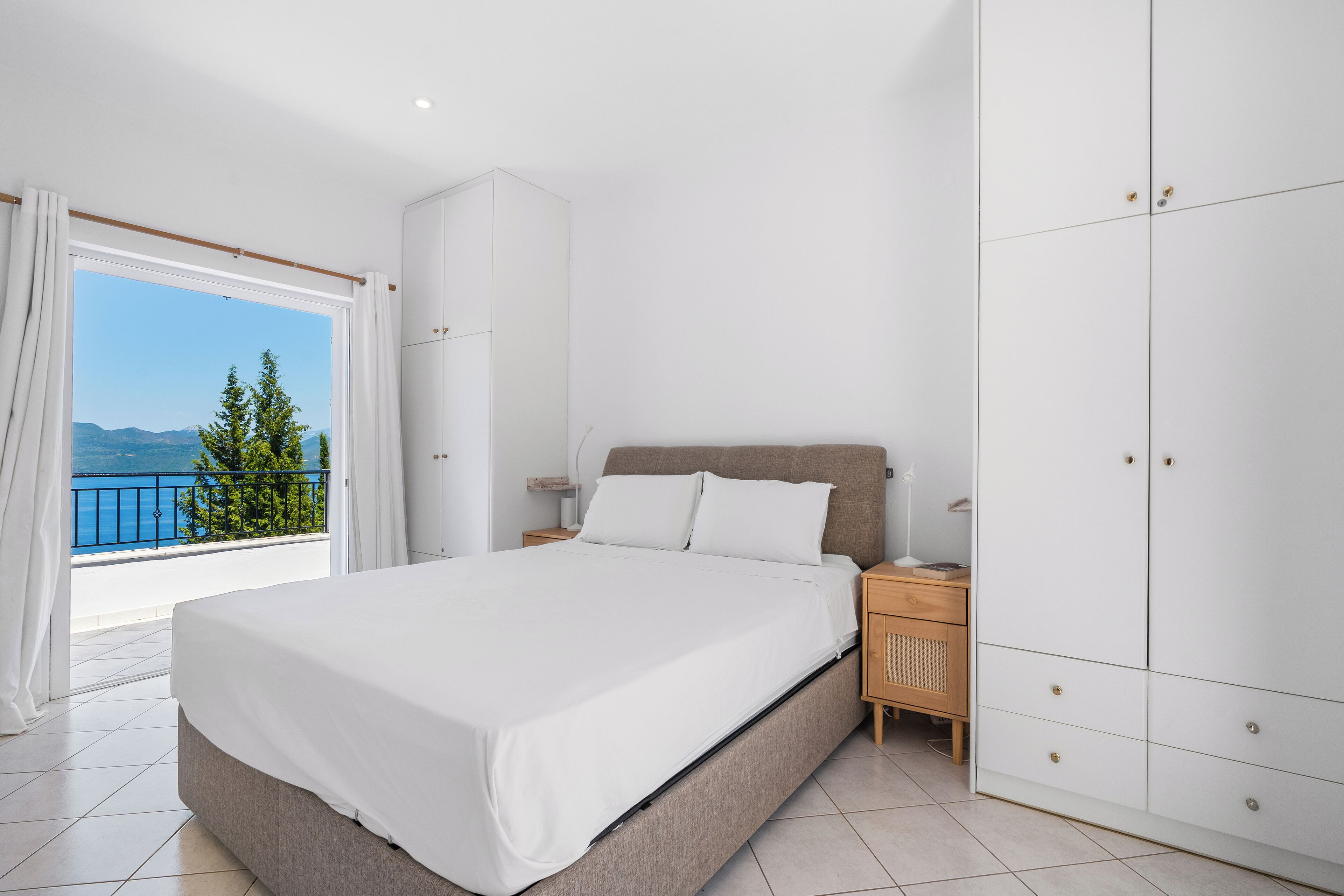 Een slaapkamer met een bed, een kledingkast, een nachtkastje en uitzicht op het landschap.