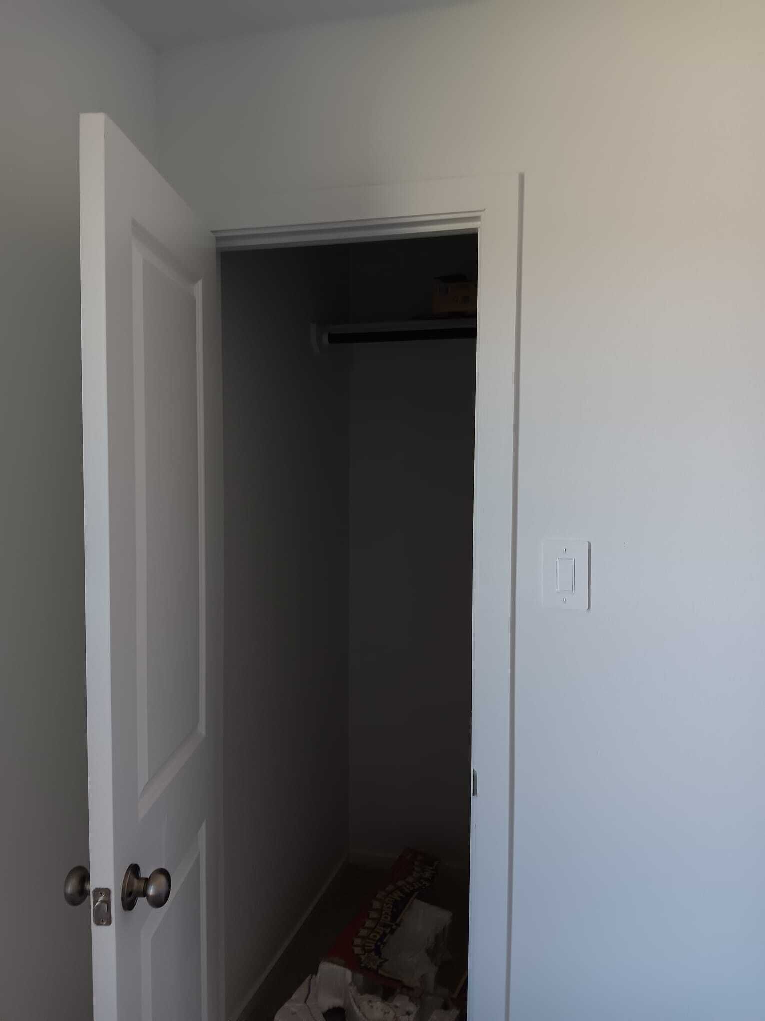 Ein schmaler Flur mit einer weißen Tür links und einem Schrank mit Kleidern rechts.