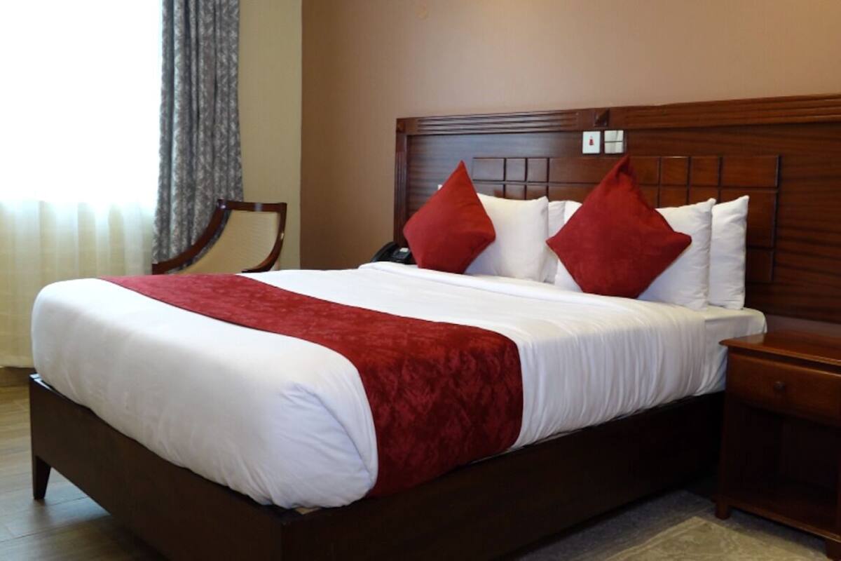 A neatly made bed with a red and white bedspread, a wooden headboard, and a nightstand with a lamp.