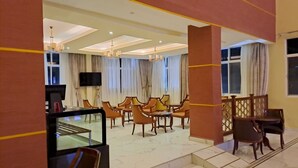 A spacious dining area with multiple wooden tables and chairs, a flat-screen TV, and large windows with curtains. - Abuya Palace Hotel Moyale (Moyale)