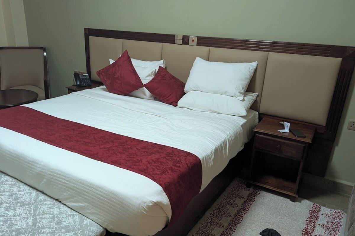 A hotel room with a large bed, a bedside table with a phone, a chair, and a small desk.