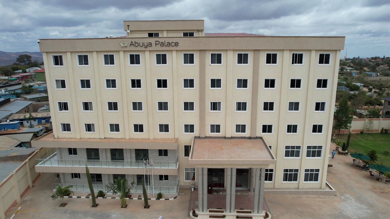 A multi-story hotel named "Abuya Palace" with a symmetrical facade, a central entrance, and a surrounding landscaped area.