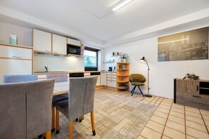 A modern kitchen with built-in appliances, a dining area with grey upholstered chairs, and a large framed cityscape on the wall. - Apartment 'Ruhige Im Schwarzwald' with Private Terrace and Wi-Fi (Pforzheim)