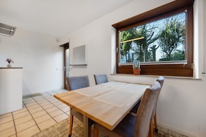 A dining area with a wooden table and chairs, a window with a view of trees, and a white wall with a mounted TV. - Apartment 'Ruhige Im Schwarzwald' with Private Terrace and Wi-Fi (Pforzheim)
