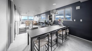Una cocina moderna con una mesa de comedor alargada, paredes oscuras y ventanas amplias que ofrecen vistas al exterior.