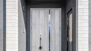 Entrada de un edificio moderno con puertas dobles, un escalón pequeño que lleva a la puerta y un suelo de baldosas claras.