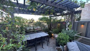 Une terrasse extérieure agrémentée d’une pergola en bois, d’une table avec des chaises et de diverses plantes en pot.