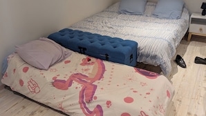 A bedroom with two beds, one with a patterned bedspread and the other with a striped one. There are pillows, a blue tufted headboard, and a nightstand with a lamp. - Chez steph (Le Puy-en-Velay)