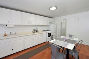 Cocina compacta con armarios blancos, estufa y lavabo. Hay una mesa de comedor con sillas y una alfombra pequeña en el suelo.