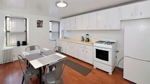 Una cocina compacta con armarios blancos, una estufa a gas, un refrigerador y una zona de comedor con mesa y sillas.