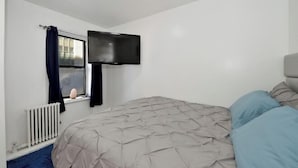Un dormitorio con cama, ventana con cortinas, televisor montado en la pared y un radiador.