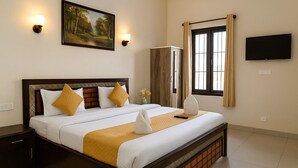 A neatly made bed with white and yellow bedding, a wooden headboard, and a painting above it. There is a wardrobe, a television on the wall, and a window with curtains. - Magnet Residency (New Delhi)