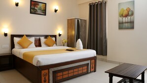 A hotel room with a bed, bedside tables, a wardrobe, a desk, and a painting on the wall. - Magnet Residency (New Delhi)