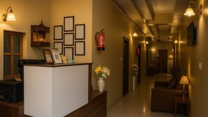 A hotel reception area with a reception desk, framed certificates, a fire extinguisher, a vase with flowers, and a couch. - Magnet Residency (New Delhi)