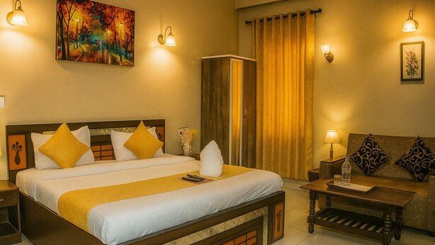 A hotel room with a large bed, a wooden nightstand, a sofa, a small table, and a painting on the wall. - Magnet Residency (New Delhi)