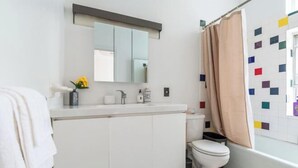A bathroom with a toilet, sink, mirror, and a shower curtain. - XL Prime Tribeca Furnished Loft (New York)