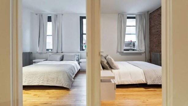 A bedroom with two beds, wooden flooring, and large windows with curtains. - XL Prime Tribeca Furnished Loft (New York)